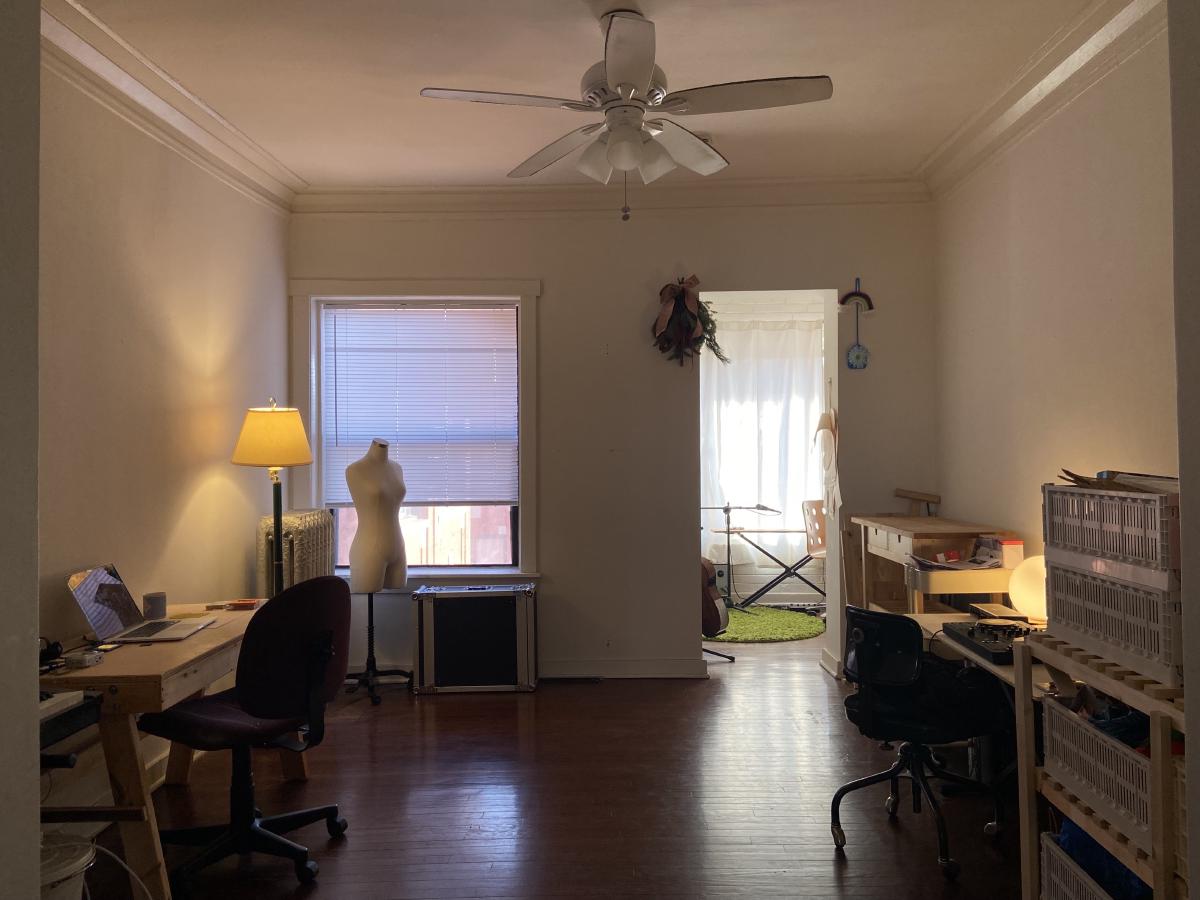 our work room with two desks two lamps shelves and the entry way to a sun room and a window the sun is setting outside